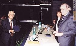 Mario Mentaschi (a sinistra) mentre riceve il premio Usfi 2004. Sul podio si vede in primo piano il presidente dell’Unione, Renato Russo; in fondo c’è il vicepresidente, Claudio Baccarin. Nel mezzo, il direttore della divisione filatelia di Poste italiane, Marisa Giannini