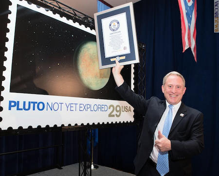 L’astronomo della Nasa Alan Stern con in mano il certificato del record. Alle spalle, l’ingrandimento della carta valore per Plutone (foto: © Usps)