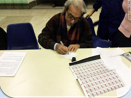 Il protagonista mentre firma autografi per i bambini. Sul tavolo, il foglio con uno dei suoi francobolli, il “Donna con liocorno” 