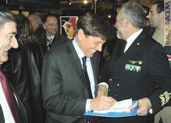 Gianni Morandi impegnato a firmare autografi con l'ammiraglio Giuseppe Lertora; a sinistra, il presidente della Federazione fra le società filateliche italiane, Piero Macrelli